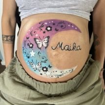 Close up of a beautifully painted baby bump, featuring moon design with delicate details. unique pregnancy belly painting in Tauranga