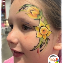 Child with a bright yellow daffodil face painting design at a Tauranga event