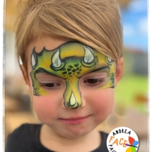 Child with a fun dinosaur face painting design at a Tauranga event